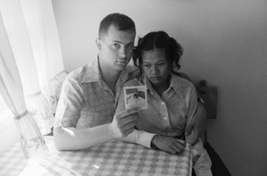 black and white: kevin's parents sit at kitchen table holding picture of kevin and looking sad